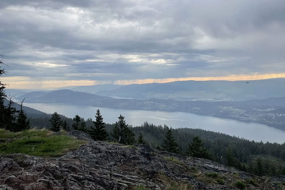 Sweeping panoramic views from the summit of Blue Grouse Mountain showcasing the Okanagan Valley stretching into the distance beneath a dramatic sky.